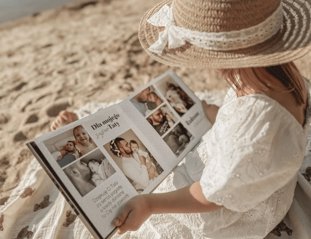 Dziewczynka na plaży ogląda fotoksiążkę ze zdjęciami z tatą